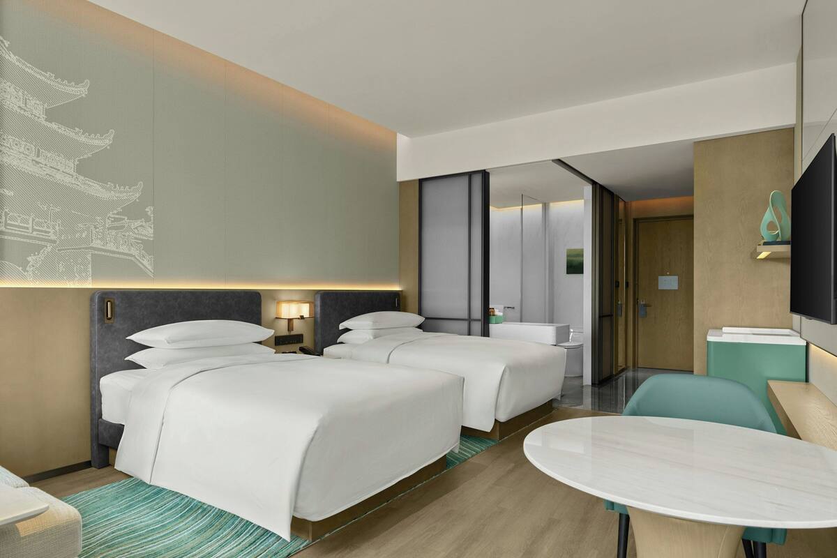 A hotel room with two beds, a sitting area with a table, a TV, and a wall with a decorative design.