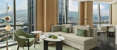 A modern hotel room with a large window, a sofa, a small table, and a chair.