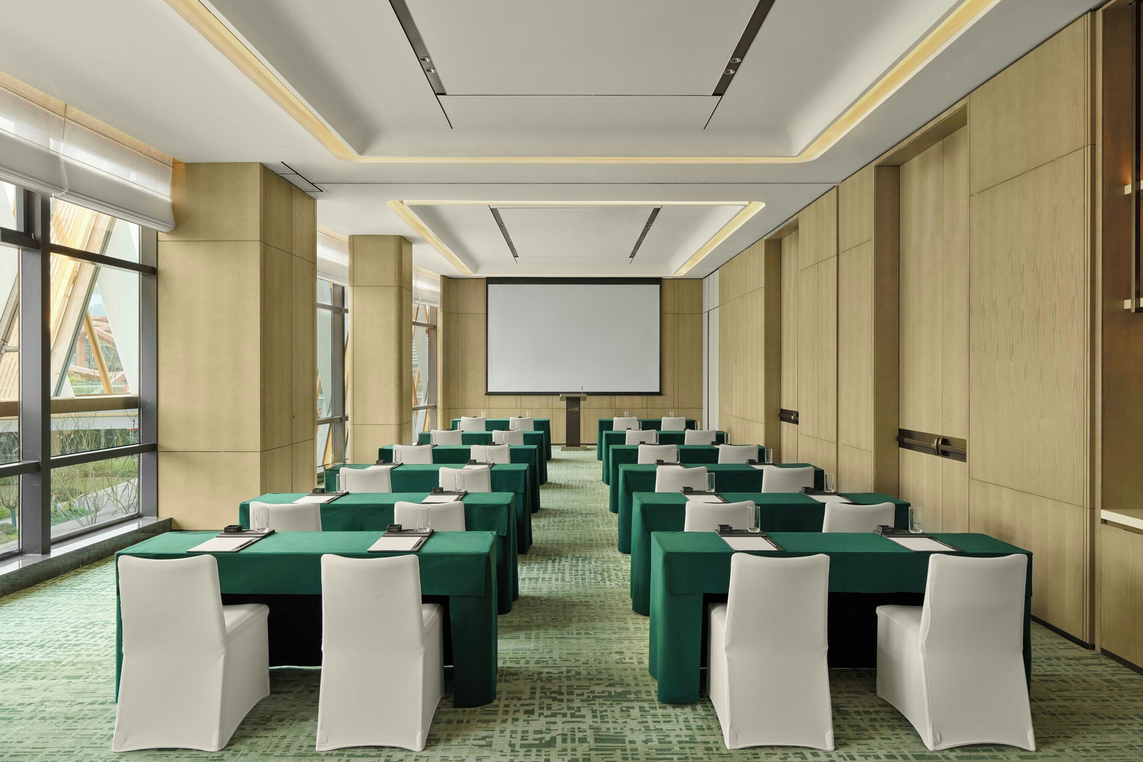 A conference room with rows of tables, chairs, and a large screen at the front.