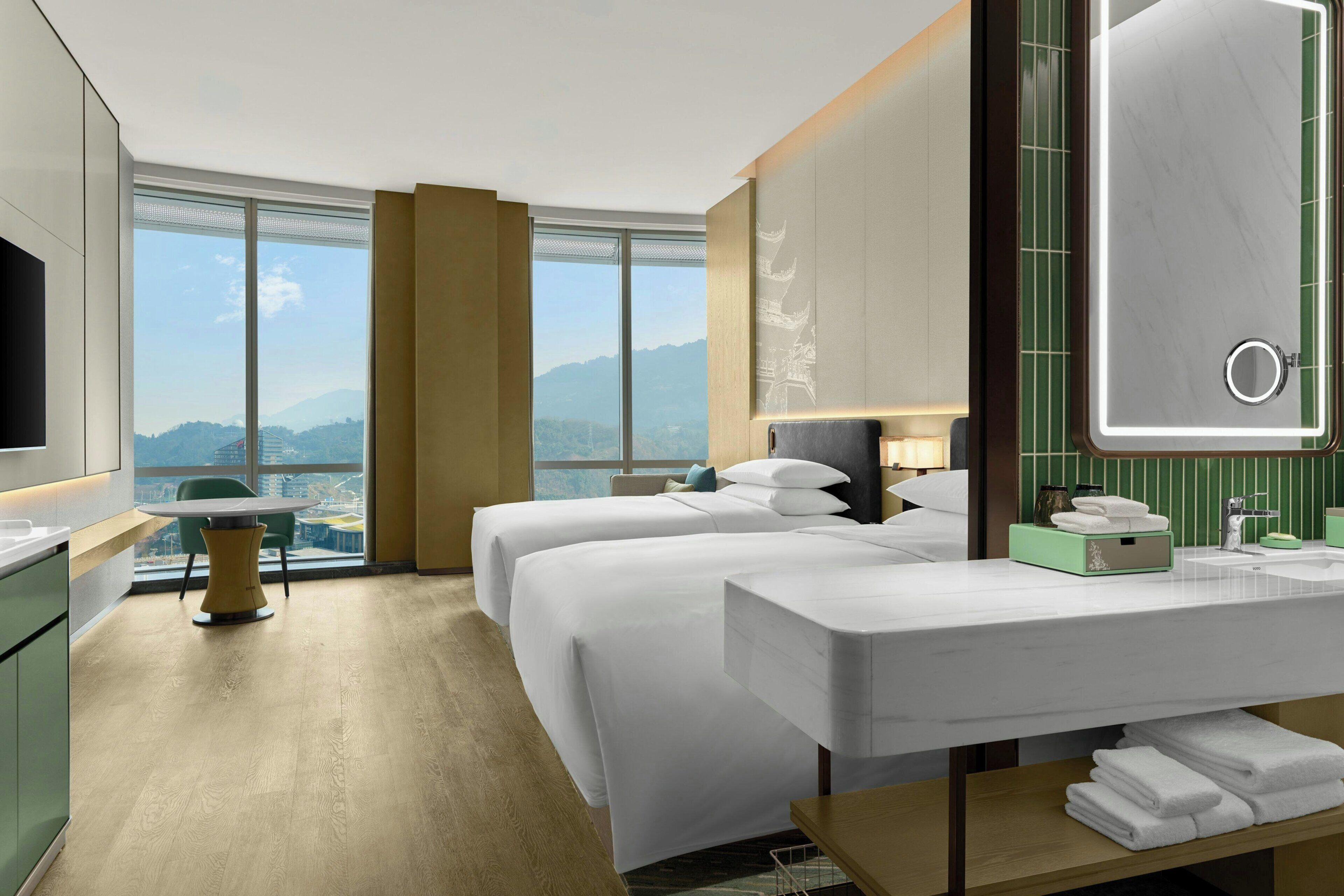 A hotel room with two beds, a large mirror, a TV, a desk, and a view of mountains.
