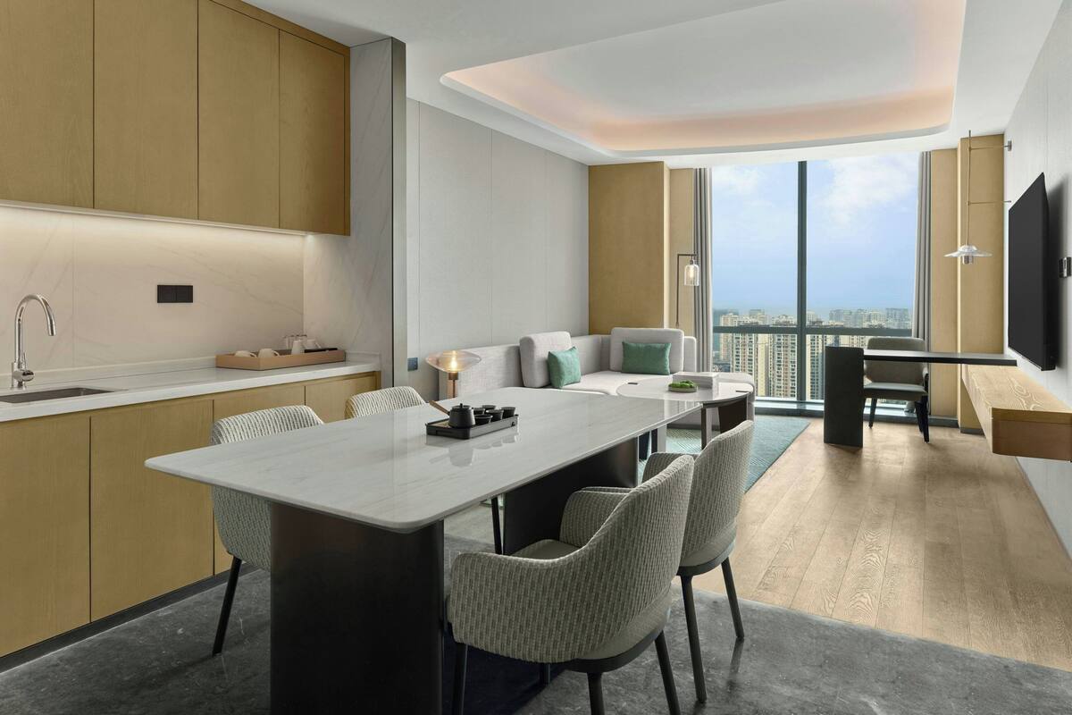 A modern kitchen with a central island, dining area with chairs, a sofa, and a TV mounted on the wall.
