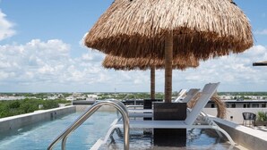 Uma piscina infinita no terraço, com um guarda-sol de palha, cadeiras de lounge e vista para a cidade.