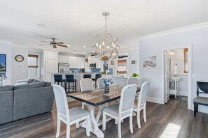 Een moderne keuken met witte kasten, een eethoek met een houten tafel en stoelen, en een grijze bank.