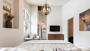 Quarto com uma cama grande, cômoda de madeira, televisão e lustre.