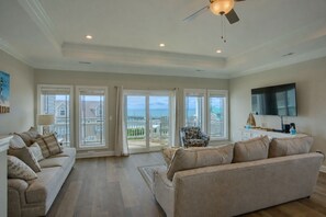 A spacious living room with a large sofa, a smaller sofa, a patterned armchair, and a television mounted on the wall.