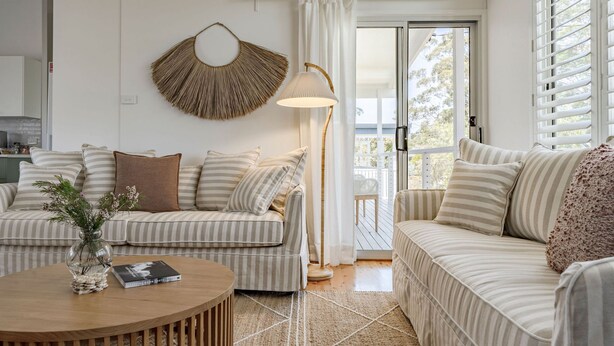 Ein Wohnzimmer mit gestreiften Sofas, einem runden Holztisch, einer Stehlampe und einem Wandbehang.