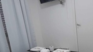 A bedroom with a bed, a flat-screen TV mounted on the wall, a door, and a window with curtains. - Hotel Tropea (Mar del Plata)