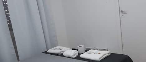 A bedroom with a bed, a flat-screen TV mounted on the wall, a door, and a window with curtains.