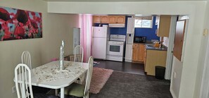 A compact kitchen with white appliances, a dining area with a table and chairs, and a pink rug.