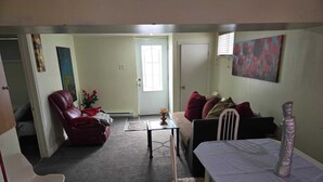 Una sala de estar con un sillón de cuero rojo, una mesa blanca, un sofá con cojines rojos y un cuadro en la pared.