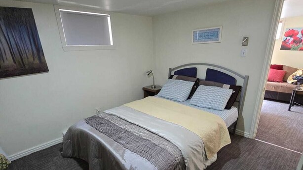 Una cama individual con cabecera, una mesita de noche, una lámpara de escritorio, una silla y una ventana pequeña.