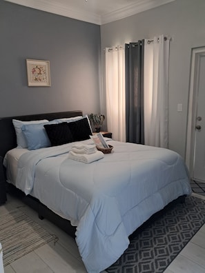 Ein ordentlich bezogenes Bett mit einer blau-weißen Bettdecke, ein gerahmtes Bild an der Wand und ein Blumentopf neben dem Bett.