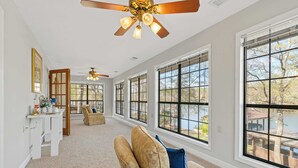 Une pièce spacieuse dotée de grandes fenêtres, d’un ventilateur de plafond et d’un coin salon confortable.