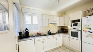 A kitchen with white cabinets, a microwave, an oven, a sink, and a kettle. - Residential neighborhood, pleasant south-facing house (FOURAS)