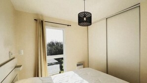 A bedroom with a bed, a window with curtains, a door, and a hanging light fixture. - Residential neighborhood, pleasant south-facing house (FOURAS)