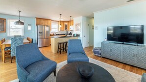 Una cocina moderna con una isla central, un comedor con mantel estampado y una sala de estar con televisor y asientos.