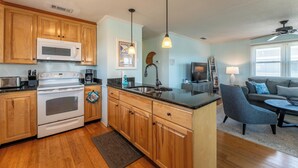 Cocina con armarios de madera, microondas, estufa y comedor con sofá y mesa de centro.