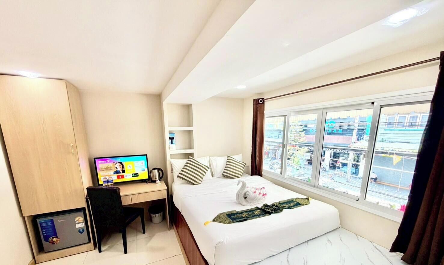 Une chambre d’hôtel comprenant un lit, un bureau avec un ordinateur, une fenêtre donnant sur la ville et une armoire.