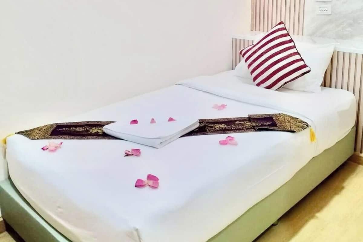 A neatly made bed with white bedding, a striped pillow, and rose petals scattered on the surface.