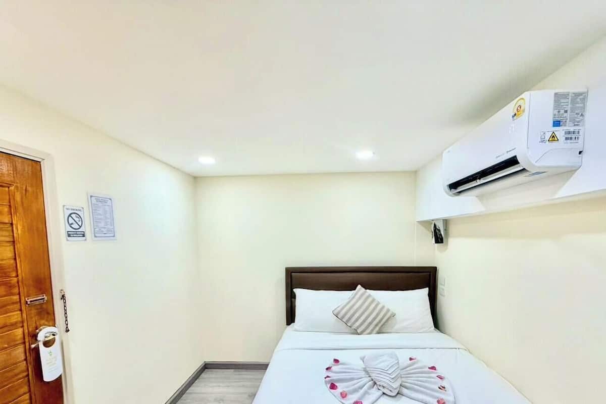 A hotel room with a bed, a wooden door, an air conditioning unit, and a wall-mounted sign.