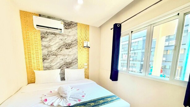 A hotel room with a bed, an air conditioning unit, a window with a view of buildings, and a curtain. - PSA Palace Khaosan (Bangkok)