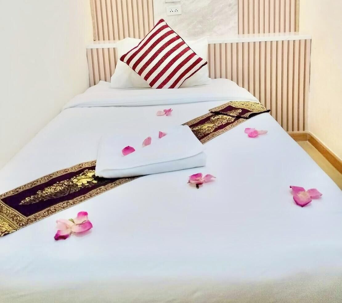 A neatly made bed with a striped pillow, a folded white towel, and scattered rose petals.
