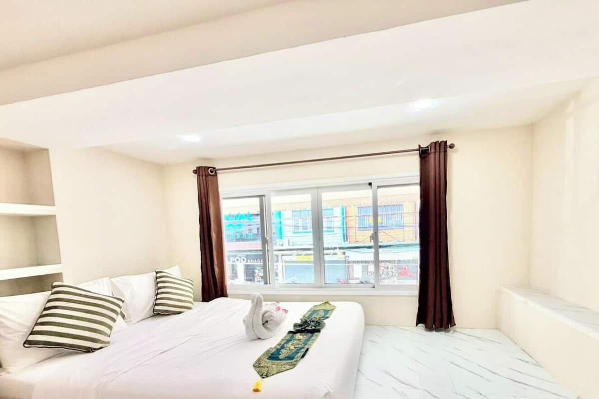 A hotel room with a bed, a window with curtains, and a view of buildings outside.