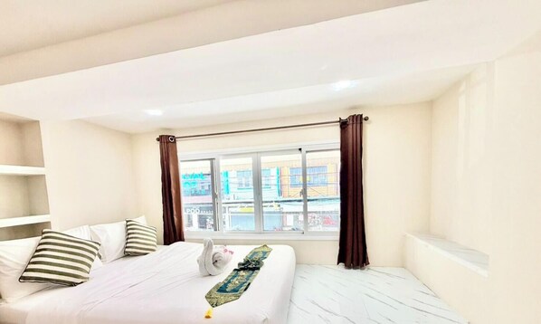 A hotel room with a bed, a window with curtains, and a view of buildings outside. - PSA Palace Khaosan (Bangkok)