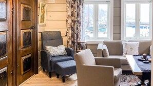 Ein Wohnzimmer mit Holztür, einem grauen Sessel, einem beigen Sofa und Blick auf einen Yachthafen durch große Fenster.