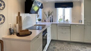 Eine moderne Küche mit weißen Schränken, einem eingebauten Backofen, einem großen Fenster mit Aussicht und dekorativen Tellern an der Wand.