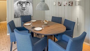 Ein Essbereich mit einem runden Holztisch, sechs blau gepolsterten Stühlen, einer Pendelleuchte und einem Wandbild eines Rams.