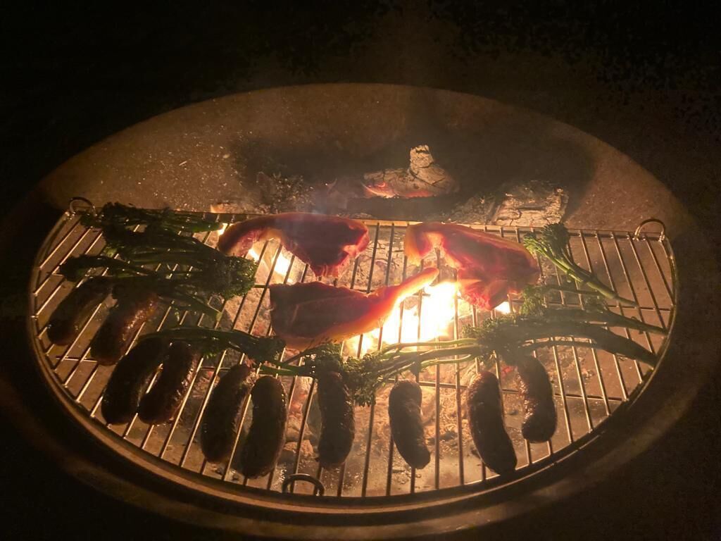 A grill with sausages and vegetables being cooked over an open flame.