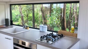 Een moderne keuken met een groot raam, roestvrijstalen apparatuur en uitzicht op het bos.