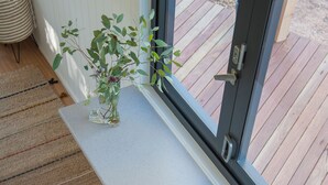Een houten terras met een witte bank en twee krukken, een glazen pot met deksel, en een rieten mand.