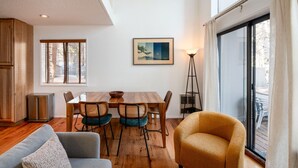 Un coin repas avec une table et des chaises en bois, un lampadaire et une grande fenêtre donnant sur les arbres.