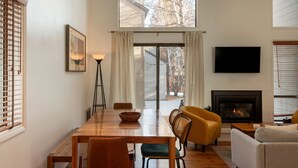 Un salon moderne avec une table à manger en bois, deux chaises, un canapé, un téléviseur et une cheminée.