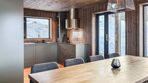 A modern kitchen with grey cabinets, a wooden dining table, and a view of a snowy mountain through large windows. - Lovely home in Bjorli with sauna (Bjorli)