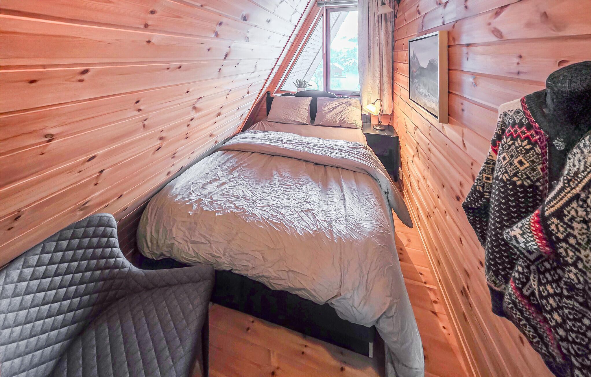 Una habitación de cabaña de madera con una cama, una ventana y un cuadro enmarcado en la pared.