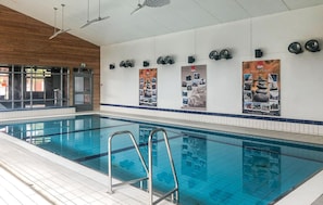 A large indoor swimming pool with clear blue water, surrounded by tiled walls and wooden paneling.