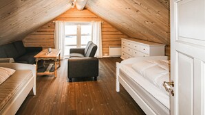Ein gemütliches Schlafzimmer im Dachgeschoss mit Holzbalkendecke, einem Bett, einem Sofa, einem Sessel und einer Kommode.
