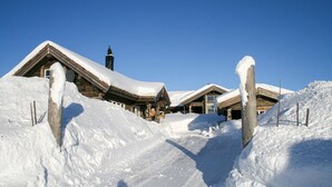Eine schneebedeckte Lodge mit mehreren Holzhäusern, klarem Himmel und verschneiter Landschaft.