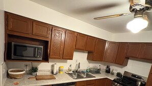 Una cocina con armarios de madera, microondas, lavavajillas, pileta y estufa.