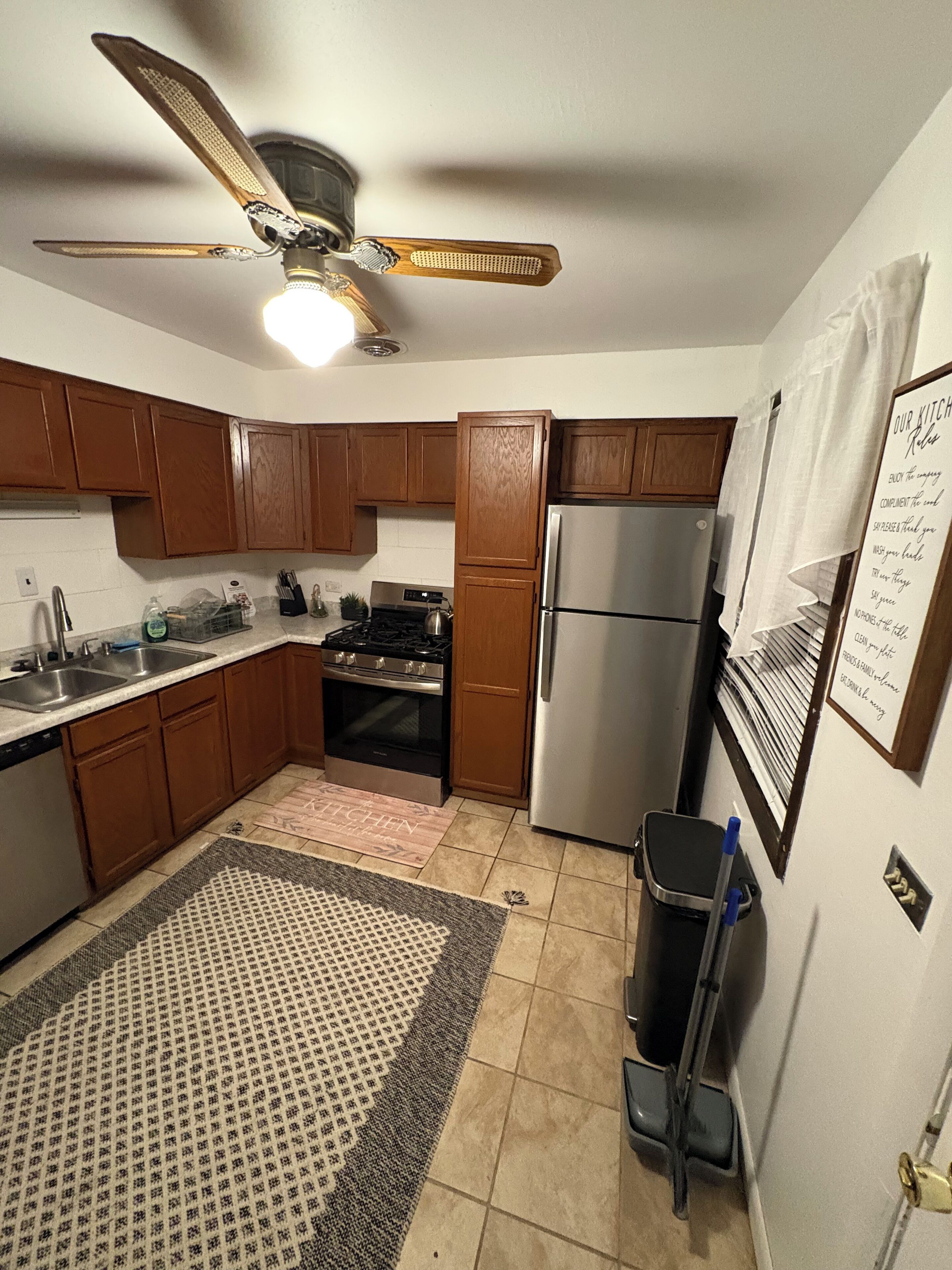 A kitchen with wooden cabinets, a stainless steel refrigerator, a gas stove, and a ceiling fan.
