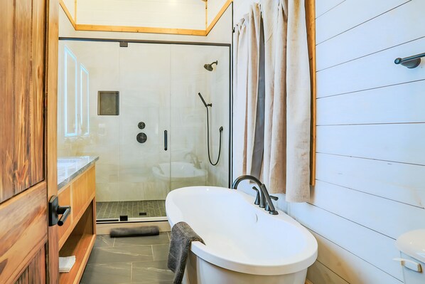 A modern bathroom with a freestanding bathtub, a glass-enclosed shower, and wooden cabinetry. - Riverside Retreat, Riverfront, Broken Bow, Sleeps 12 (Broken Bow)