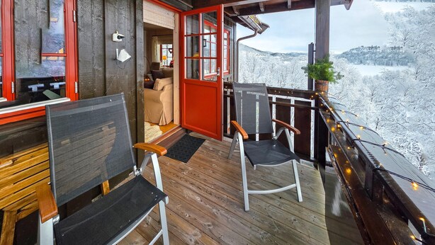 En träveranda med två stolar och en soffa, en röd dörr och utsikt över ett snötäckt landskap.
