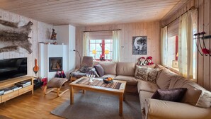 Ett mysigt vardagsrum med en soffa, en fåtölj och ett soffbord. Här finns också en öppen spis, en tv och en upphängd djurhud.