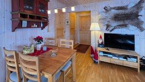 En inredning med träpanel, ett matbord, stolar, en tv och ett upphängt djurhuvud eller skinn.