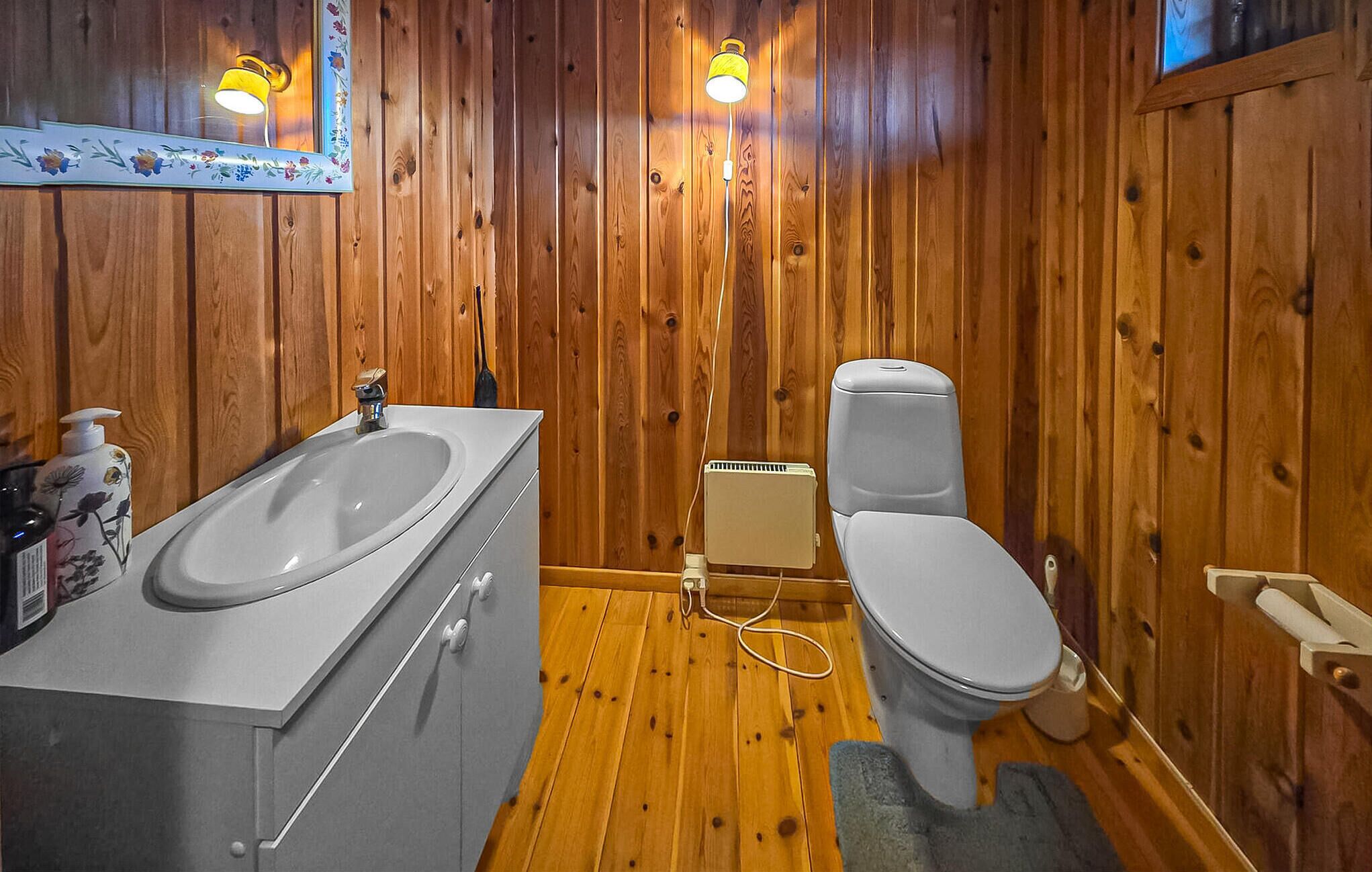 A wooden-paneled bathroom with a white sink, a toilet, and a heater.