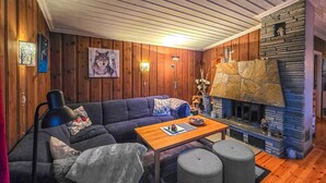 A cozy living room with a stone fireplace, wooden walls, a sofa, and a coffee table.