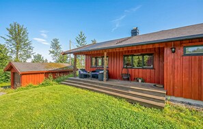 A red wooden cabin with a covered porch, a small shed, and a well-maintained lawn.